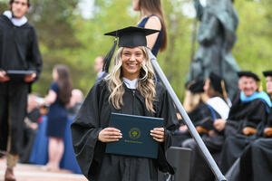 Female graduate wearing a black cap and gown holding her diploma folder.
