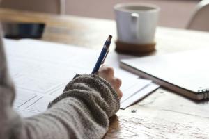 A hand holding a pan and writing in a notebook