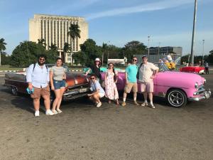 Students posing with classic cars during a trip to Cuba