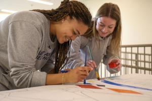 Two students working on art for a mural