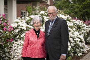 Woman and man stand in front of flowers and a building.