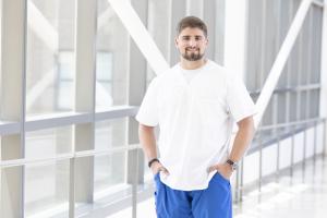 Male nurse stands in a hospital structure wearing a white shirt and blue scrubs