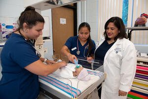 Two female student nurses and a female nurse instructor in a SIM lab with an infant manikin