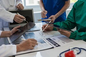 Medical professionals working with tablets, laptops, papers, and clipboards