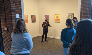 Student in front of displayed artwork speaks to a group  