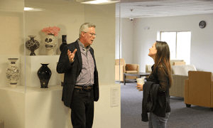 Professor Gary Bouchard speaks with a woman in front of a display case of vases