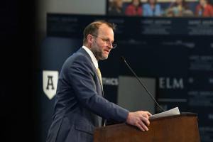 Max Latona speaking behind a podium at the forum