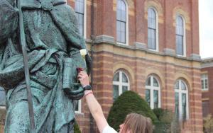 Student putting a flower in the arm of St. Anselm