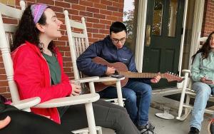 Student playing guitar on the Joseph Hall porch while others listen