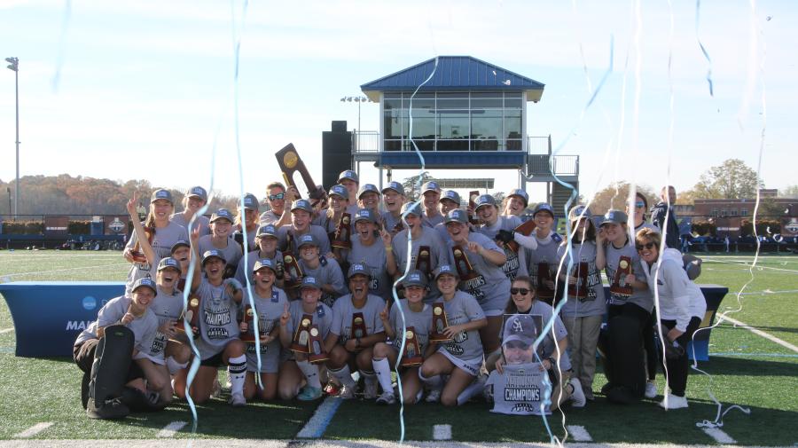 Group of women field hockey players pose with trophies as streamers fall from above.